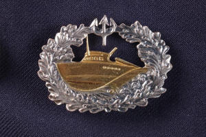 Gold- und Silbernes Abzeichen der deutschen Marine mit einem Boot, auf einem Tuch dargestellt.