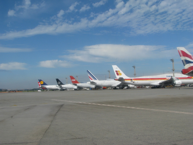 Eine Rollbahn mit wenigen Flugzeugen, Masten, Kabeln und einer bew├Âlktem Himmel.