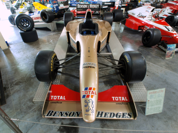 Rennwagen in einem Motorsportmuseum ausgestellt, durch einen Metallzaun von Besuchern im Hintergrund getrennt.