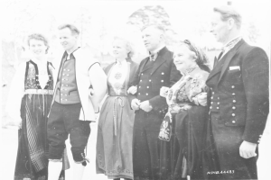 Eine Gruppe von Menschen in Schwarz-Weiß-Kleidung, die zusammenstehen, lächeln und vor Bäumen posieren, mit dem Text "Bayerische Familie in den 1930er Jahren" unten.