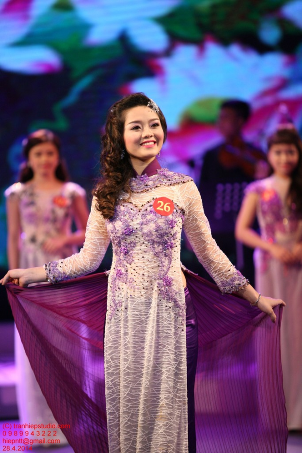 Eine Frau in einem cremefarbenen und violetten Kleid mit einer Anstecknadel darauf, mit einem unscharfen Hintergrund.