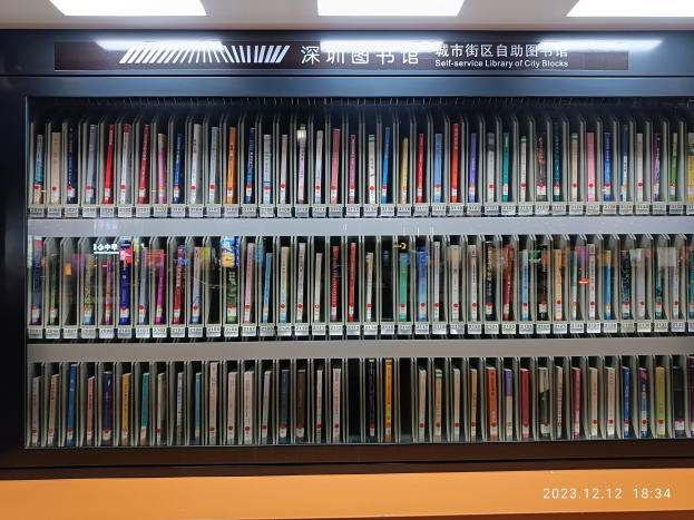 Eine gut beleuchtete Bibliothek mit Reihen von Bücherregalen, einer Tafel mit Text und einem Wasserzeichen unten, ähnlich einer Selbstbedienungsbibliothek der Stadtblöcke.