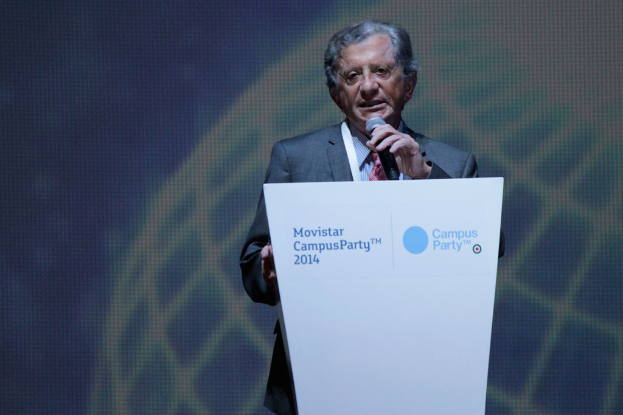 Eine Person steht an einem Podium mit einem Mikrofon, spricht, mit einem digitalen Bildschirm mit Text dahinter.