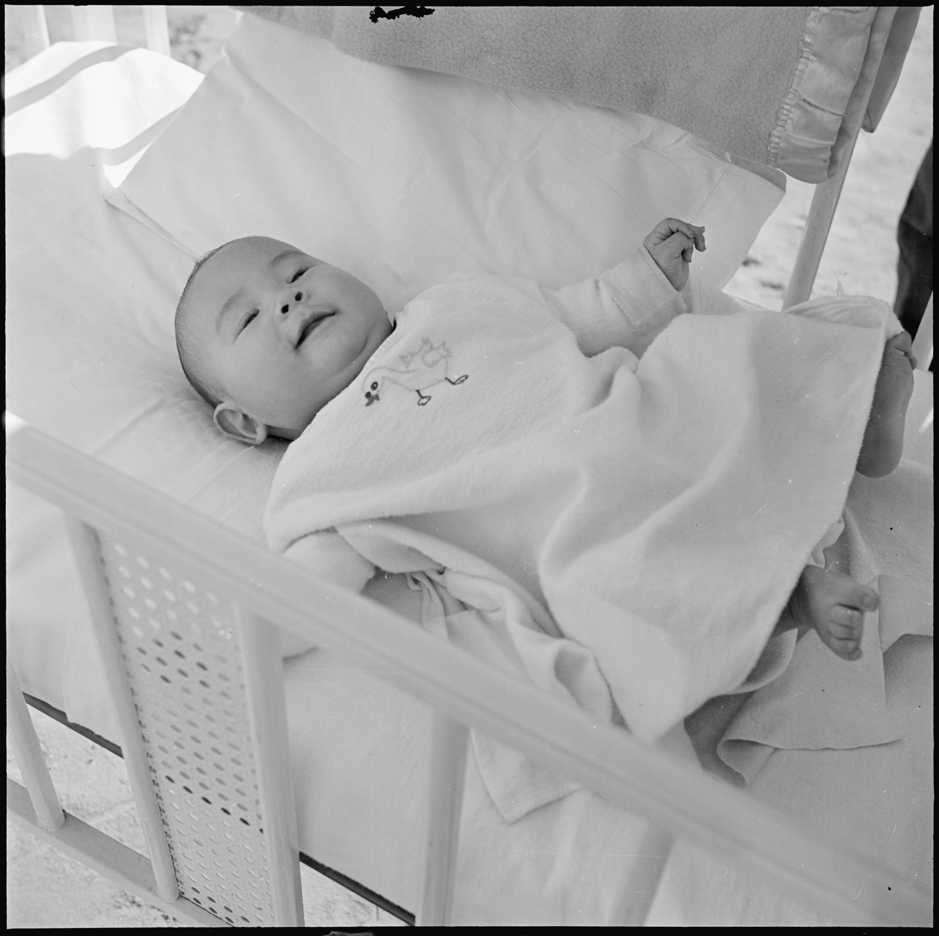 Ein Schwarz-Weiß-Foto eines Babys, das friedlich in einer Wiege schläft, eingewickelt in eine Decke.