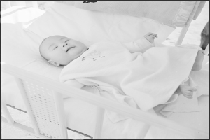 Ein Schwarz-Weiß-Foto eines Babys, das friedlich in einer Wiege schläft, eingewickelt in eine Decke.