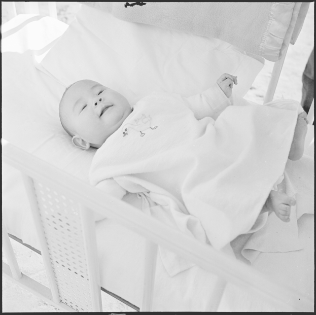 Ein Schwarz-Weiß-Foto eines Babys, das friedlich in einer Wiege schläft, eingewickelt in eine Decke.