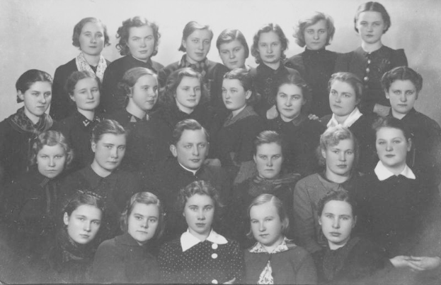Ein Schwarz-Weiß-Foto einer Gruppe von Frauen in Schuluniformen vor einer Wand mit der Aufschrift "1918-1918 Schulmädchen" am unteren Rand.