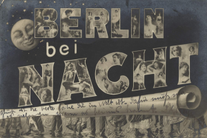Schwarzes und weißes Foto einer Gruppe von Menschen, die vor einem Schild mit der Aufschrift "Berlin Bei Nacht" mit einem Mond im Hintergrund stehen, einige lachen und feiern, unter einem festlichen, stern- und streifenförmigen Schild.