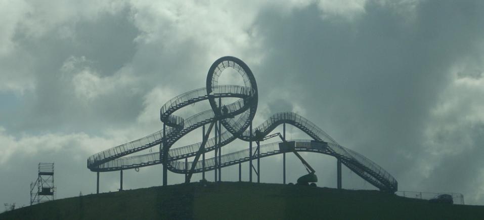 Eine Achterbahn auf einem Hügel mit einem bewölkten Himmel im Hintergrund, umgeben von Stützpfählen und -strukturen.
