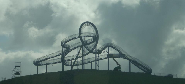 Eine Achterbahn auf einem Hügel mit einem bewölkten Himmel im Hintergrund, umgeben von Stützpfählen und -strukturen.