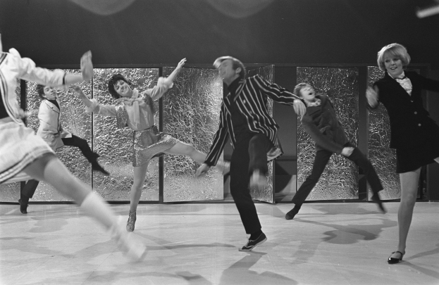 Eine Gruppe von Menschen, die auf einer Bühne tanzen, in Schwarz-Weiß mit einer Wand im Hintergrund und mit Schuhen.
