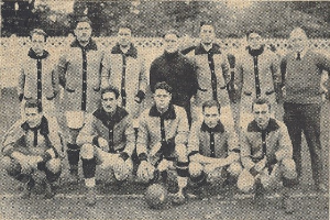 Ein Schwarz-Weiß-Foto einer Fussballmannschaft, bei dem einige Spieler stehen und andere in einer Hockposition sind, mit Text unten.