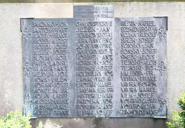 Ein Steinplaque an einer Wand mit eingravierten Text, umgeben von Pflanzen unten, wahrscheinlich ein Holocaust-Mahnmal.