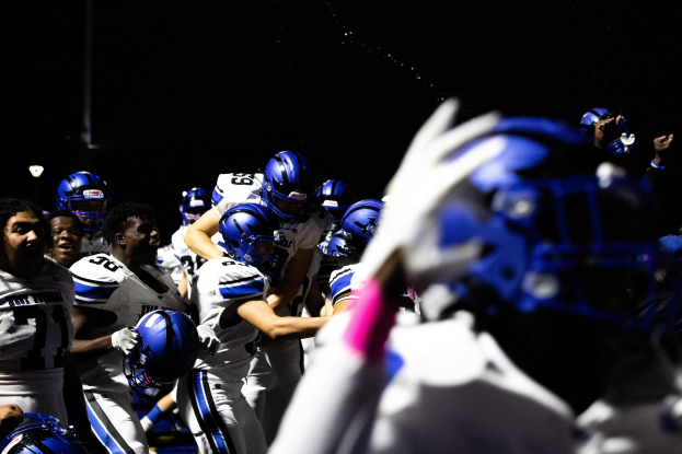 Gruppe von Fußballspielern in weißen Uniformen und blauen Helmen auf dem Feld zusammengedrängt.