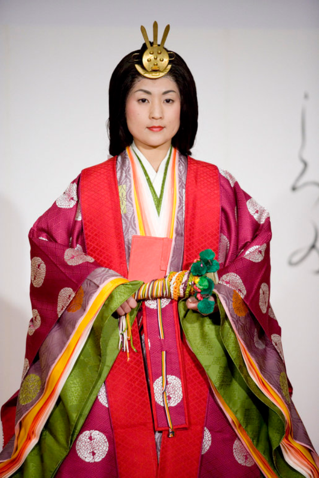 Eine Frau in einem traditionellen japanischen Kimono, das ein leuchtend rotes und grünes Kleid mit aufwändigen Mustern ziert, posiert selbstbewusst auf einem Laufsteg mit einem ordentlichen Dutt.