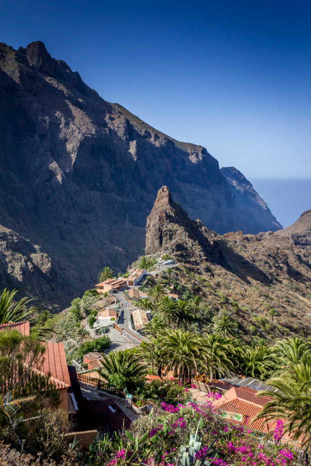 Eine Landschaftsaufnahme mit Häusern, Bäumen und Felsen in der Mitte, mit einem Hügel und Himmel im Hintergrund.