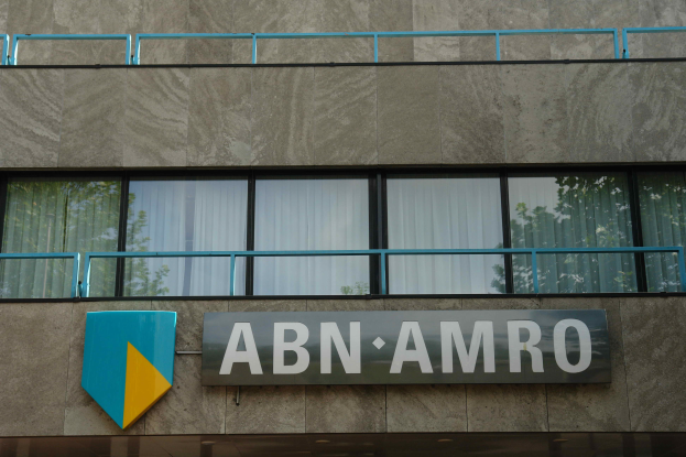 Ein Gebäude mit "ABN AMRO"-Schriftzug, ein Schild, das darauf hinweist, dass es der Hauptsitz ist, Geländer und Glasfenster mit Vorhängen, mit Text unten, der eine Strafe von 1,5 Milliarden Dollar durch die Europäische Union erwähnt.