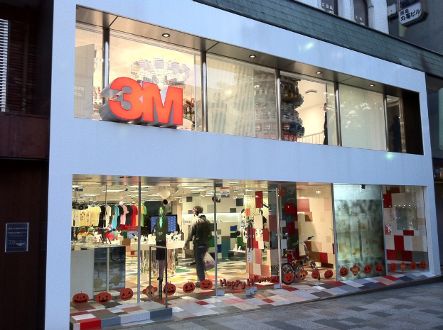 Ein Gebäude mit einer Glaswand, die Kleider an Bügeln, eine Schaufensterpuppe, ein Fahrrad und Schrift auf der Glaswand zeigt.