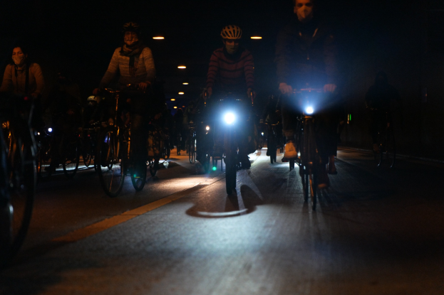 Eine Gruppe von Menschen, die nachts auf Fahrrädern durch eine Stadtstraße fahren und alle Helme tragen.