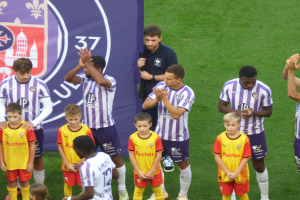 Eine Gruppe junger Jungs auf einem Fußballfeld, die klatschen, mit einem Banner und Logos im Hintergrund.