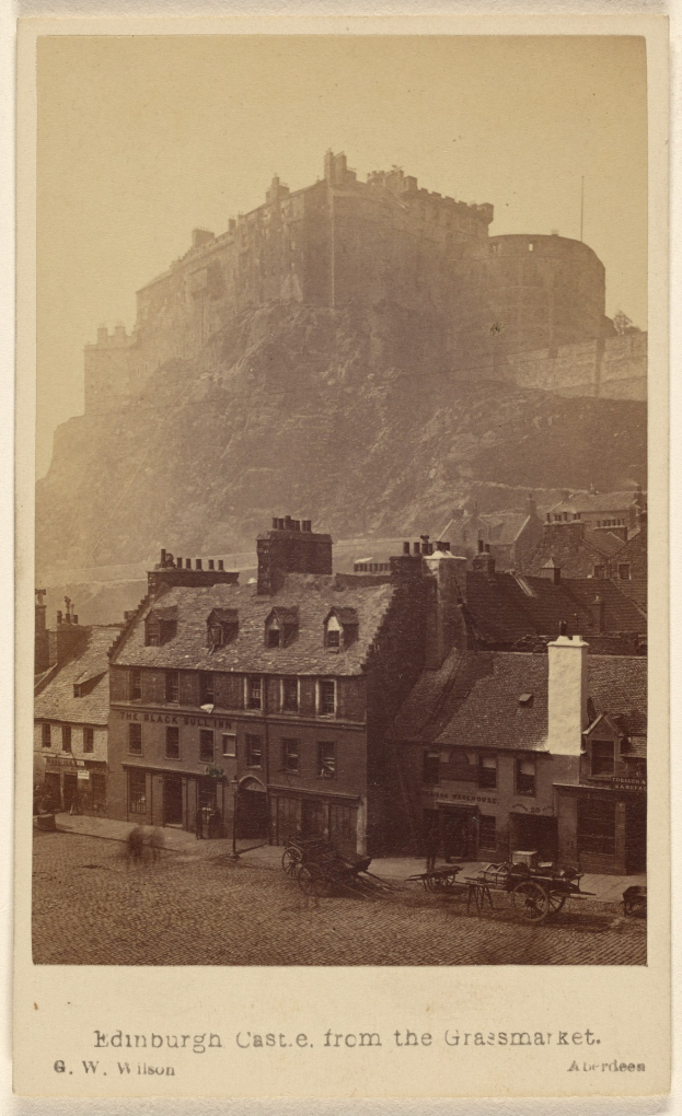 Alte Fotografie von Edinburgh Castle aus der Grassmarket-Sicht, mit Gebäuden und Karren im Vordergrund, einem Hügel im Hintergrund und Text am unteren Rand.