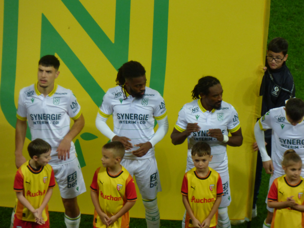 Eine Gruppe junger Jungs auf einem Fußballfeld neben einem bunten Banner, auf dem "Ligue 1 - Olympique Lyonnais" steht.