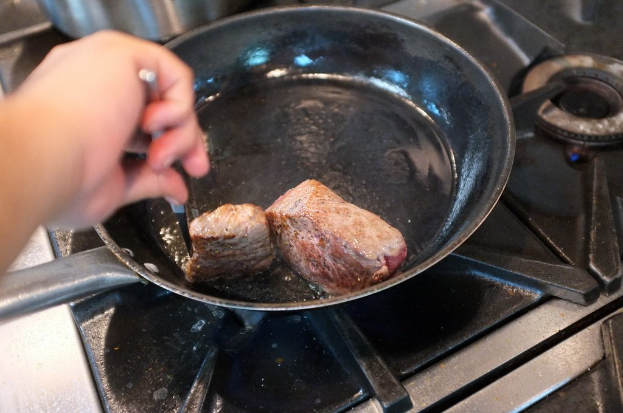 Eine Hand hält ein Objekt in der Nähe eines Herdes mit Utensilien und einem Topf mit Lebensmitteln.