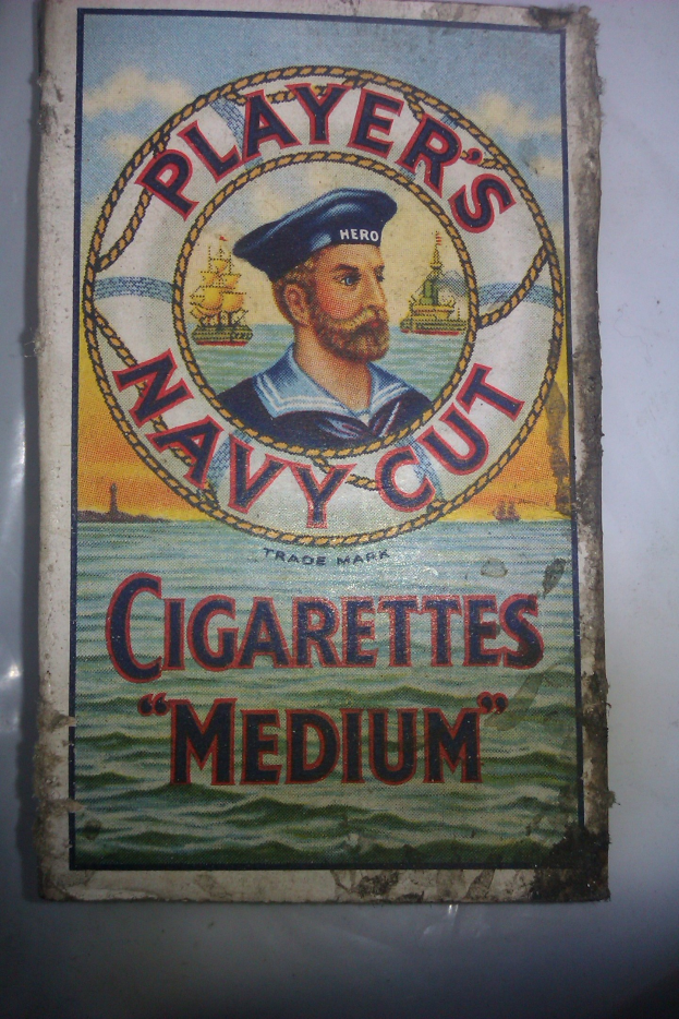 Plakat, das "Player's Navy Cut Cigarettes Medium" bewirbt, zeigt eine Person in einer marineblauen Uniform mit weißem Hemd und roter Krawatte, die Arme verschränkt und einen strengen Gesichtsausdruck hat, mit fetter schwarzer Schrift in einem weißen Rahmen.
