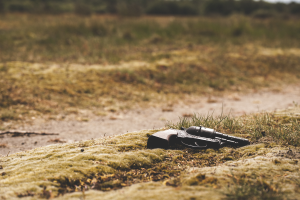 Eine Waffe liegt auf dem Boden in einem grasbewachsenen Feld, umgeben von Bäumen mit einem unscharfen Hintergrund.