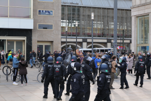 Gruppe von Polizisten mit Helmen vor einer Menge mit Fahrrädern, mit Glasgebäuden, Laternen und Fahrzeugen im Hintergrund.