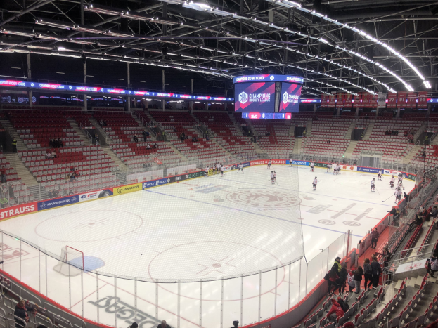 Ein Eishockeyspiel in einer großen Arena, mit Zuschauern auf den Sitzen und Stehplätzen, einem Zaun um die Eisfläche, einem Display mit der Aufschrift "St. Louis Blues vs Detroit Red Wings", Metallrahmen und einer Decke mit Deckenleuchten.