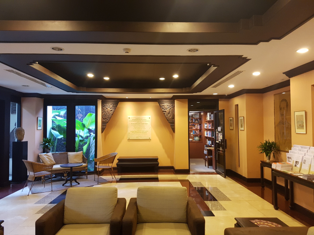 Eine Hotellobby mit Sitzbereichen, Tischen, Zimmerpflanzen, Bücherregalen, Leuchten, Wanddekorationen und Beistelltisch-Dekorationen, mit natürlichem Licht durch Fenster und Türen.