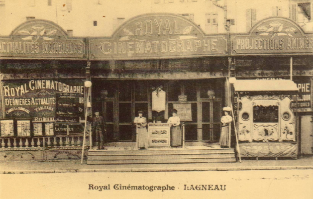 Ein altes Schwarz-Weiß-Foto des Royal Cinematographe in Ligneau, Frankreich, mit ein paar Menschen vor dem Gebäude, das mit Schildern und Lichtern geschmückt ist, und Text am unteren Rand des Bildes.