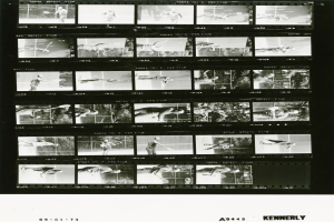 Schwarzes und weißes Foto eines konzentrierten männlichen Tennisspielers in einem weißen Hemd und Shorts, der einen Schläger hält, mit einem Filmstreifen-Hintergrund.