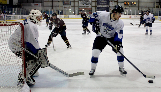Eine Gruppe junger Männer, die auf einem Eisstadion Eishockey spielen, mit Helmen und Hockeystöcken, einem Torpfosten links und Bannern im Hintergrund.