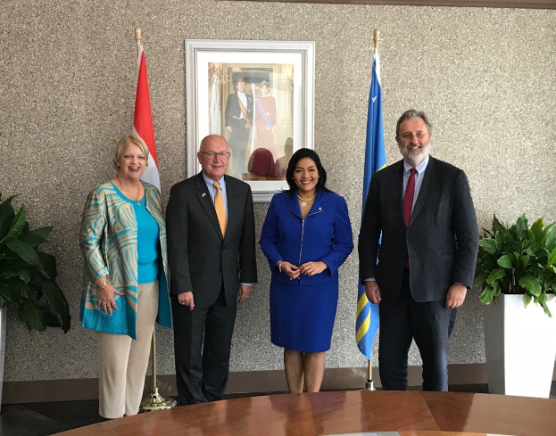 Gruppe von Menschen, die um einen Tisch mit Papieren stehen, umgeben von Fahnen, Topfpflanzen und einem Rahmenfoto an der Wand, wahrscheinlich bei der Unterzeichnung eines U.S.-Kanada-MOU feiern.