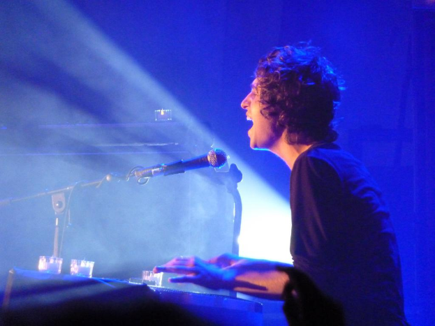 Eine Person in einem schwarzen T-Shirt DJs mit einem Mikrofon vor sich, unter blauer Beleuchtung.