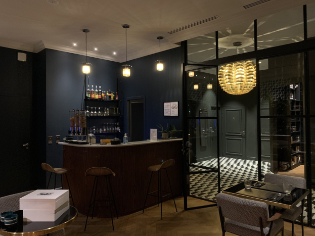 Ein privater Lounge-Bereich in Paris mit einer Bar, Hockern, Tischen, Gläsern, einer Plattform mit Flaschen, Deckenleuchten, Türen und einer Schiefertafel.