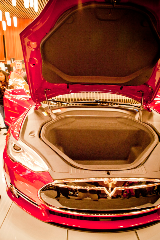 Ein Kofferraum ist offen, mit Menschen drumherum und elektrischen Lampen an der Decke.