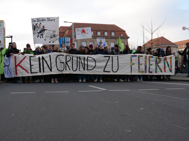 Demonstranten mit einem Banner mit der Aufschrift "Kein Grund zu Feiern" gegen deutsche Sparmaßnahmen vor einem Gebäude.