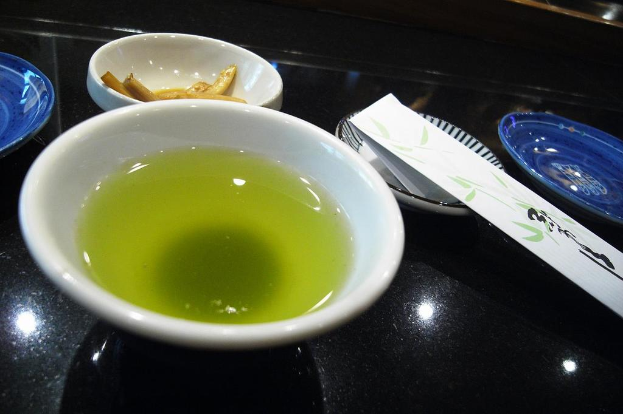 Ein schwarzer Teller mit einem Teller mit Lebensmitteln, einer Schüssel Suppe und einem nicht identifizierten Objekt.