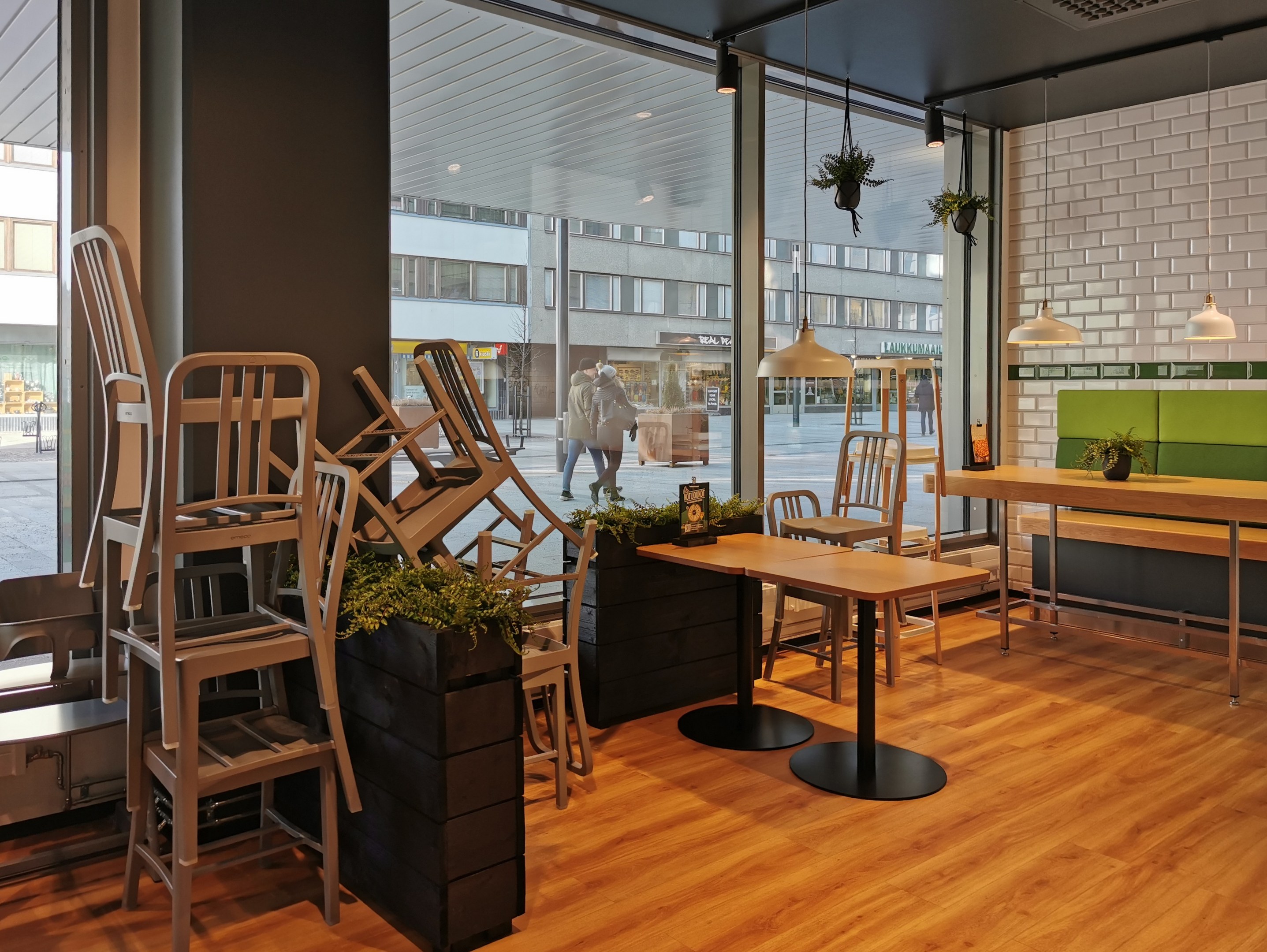 Ein Berliner Restaurant mit Holztischen und -stühlen in der Nähe eines großen Fensters, das eine Außenansicht mit Fußgängern, Gebäuden und städtischen Elementen zeigt.