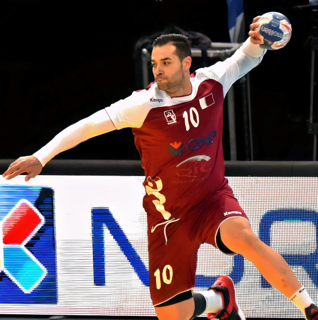 Ein Mann in einem rot-weißem Trikot spielt Handball und hält den Ball mit ausgestreckten Armen und entschlossener Miene, vor einem Hintergrund mit einer Tafel "QNP Handball-Weltmeisterschaft 2019".