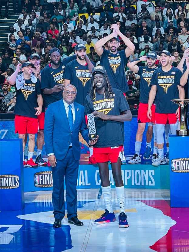 Männer mit Auszeichnungen auf einem Basketballfeld mit Zuschauern im Hintergrund und zwei Auszeichnungen auf Podesten.