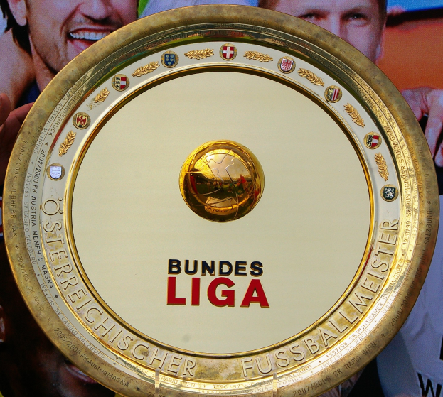 Goldener Schild mit 'Bundesliga'-Text in der Hand eines Mannes, im Hintergrund ein Banner mit drei Personen.