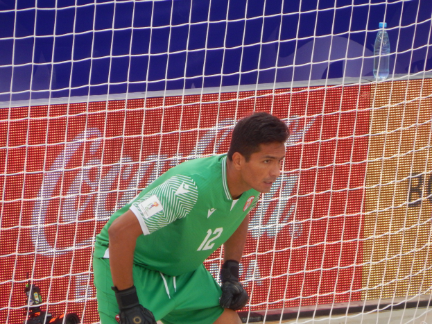 Ein Mann in grüner Torwartuniform kniet vor einem Tor mit einem Netz dahinter und einer Flasche rechts daneben.
