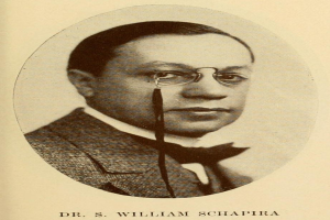 Ein Schwarz-Weiß-Foto von Dr. S. William Schapira in einem Blazer mit Brille, mit Text am unteren Bildrand.