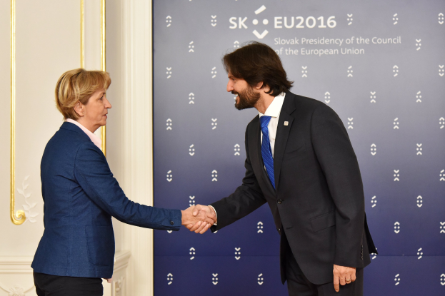 Bundeskanzlerin Angela Merkel und Bundeskanzler Joachim Gauck schütteln sich lachend vor einem "EU-Gipfel"-Schild mit einer Tür im Hintergrund die Hände.