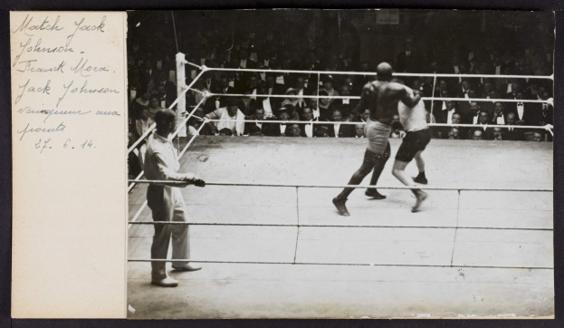 Schwarz-weiß-Foto von zwei Boxern im Ring, ein Schiedsrichter links und Zuschauer im Hintergrund, mit "Jack Johnson vs Frank Morgan"-Text in der oberen linken Ecke.