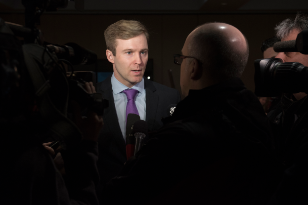 Ein Mann im Anzug und Krawatte spricht zu Reportern, flankiert von zwei Kameramännern.